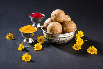 Huldi or turmeric and kumkum or kum kum with tilgul laddu or laddoo in silver bowl, sweet dish in...