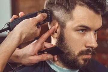 Foto op Plexiglas De handen van een jonge kapper die een kapsel maakt voor een aantrekkelijke man in de kapperszaak © master1305
