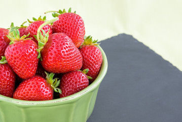Fresh picked strawberries in a green bowl on a slate platter
