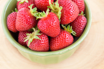 Fresh picked strawberries in a green bowl on a wood platter
