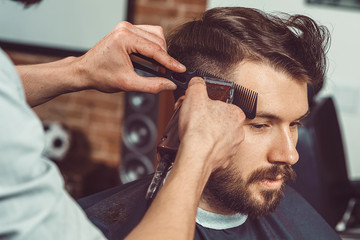 The hands of young barber making haircut to attractive man in barbershop