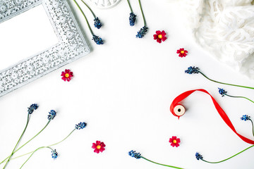 flat lay composition with flowers and decor: muscari, photo frame, white dress, spool with red ribbon