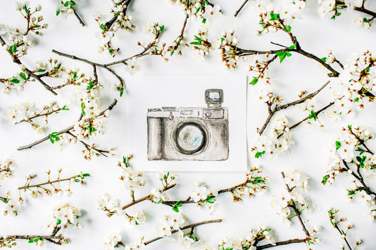 Watercolor painting of retro photo camera with branches and flowers on white background. Flat lay, top view. wreath frame