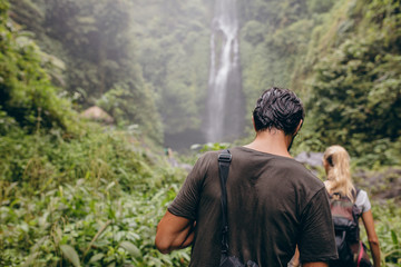 Naklejka premium Couple of tourists walking towards a waterfall in forest