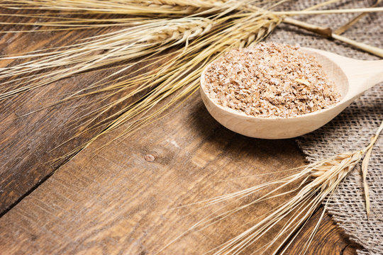 Wheat bran in wooden spoon with wheat ears