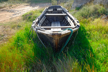 Old wooden fishing boat on the ground in tall grass in the center of composition.
