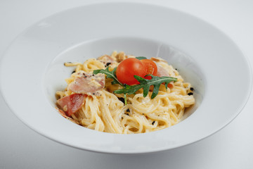 Pasta in white plate with tomatoes, greens and meat