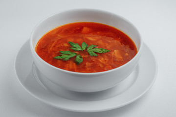 Red soup with greens in a white plate on a white background