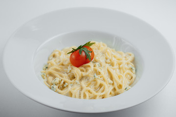 pasta with tomatoes, greens and cheese in a white plate on a white background