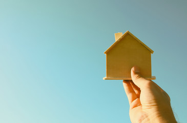 Man's hand holding a wooden toy house against blue sky