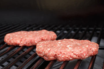 Raw hamburger patty on gas grill