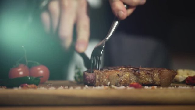 Man cuts off a piece of beef steak in a steak bar or restaurant. Close up