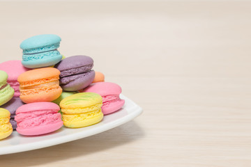 Stack of colorful macaroons cookies in dish on wood background w