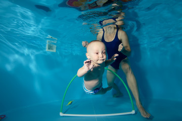 Happy baby trains with his mother underwater in the pool and swim through the Hoop. Portrait. Close-up. Horizontal orientation
