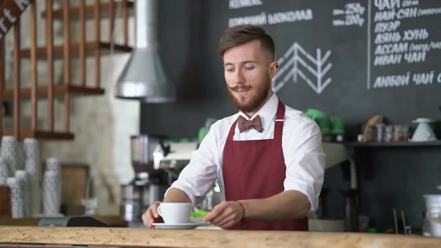 Young waiter prepares coffee at cafe
