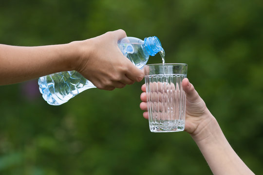 hand pouring water from bottle into glass on nature background