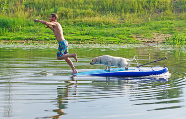 The young man and dog in the boat. The  jumps from the  in water.