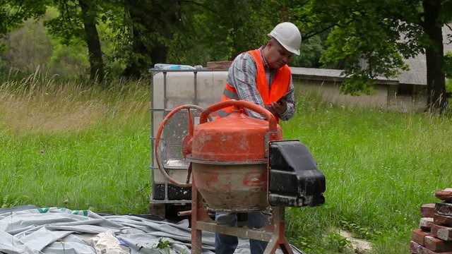 Construction worker using tablet PC near concrete mixer