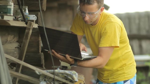 A man working on a laptop, puts aside the computer and begins sawing metal with angule grinder. Flying sparks