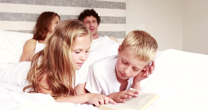 Siblings reading book on bed