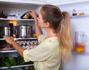 Cheerful woman searching in refrigerator