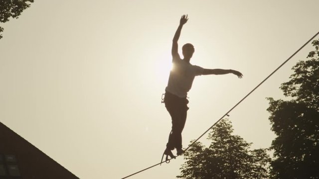 SLOW MOTION: Young man walking on slackline at golden sunset