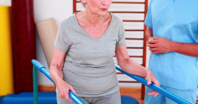 Physical therapist watching patient walk with parallel bars