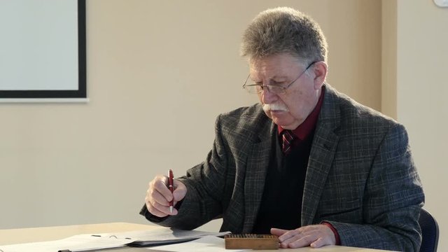 Older businessman with documents and wooden abacus