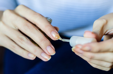 Woman with long fingers and nails applying transparent nail base at home, close up photo