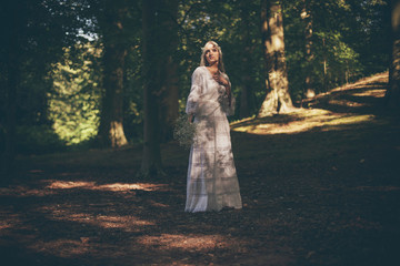 Fototapeta premium Single bride in dappled sunlight of forest