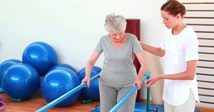 Physical therapist helping patient walk with parallel bars