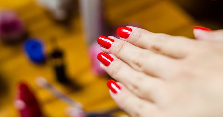 Woman with long fingers painting her long nails with red nail enamel at home, close up photo