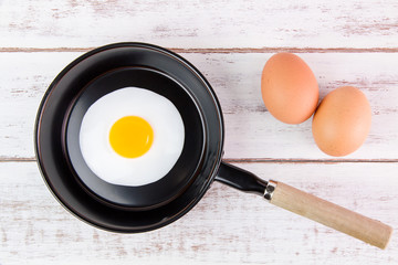 Fried egg in small pan with handle on blue wooden board
