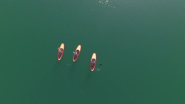 AERIAL: Flying directly above three surfer girlfriends SUP paddling on the water