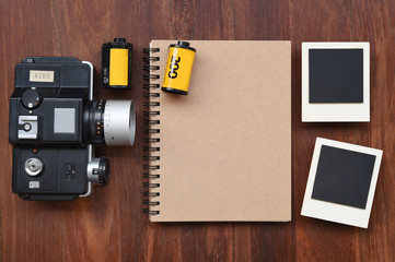 Blank notebook with photo film, photo frames and camera on wooden background