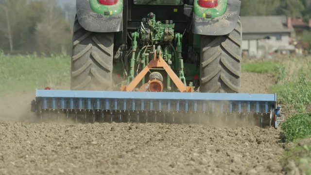 CLOSE UP SLOW MOTION: Tractor harrowing the field in spring