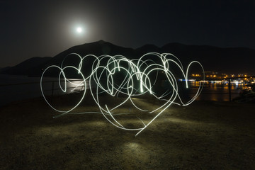 Light painting heart shapes over mountains, sea and night town background. Love. Night.