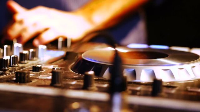 Hands of DJ tweak various track controls on DJ mixer console at nightclub.