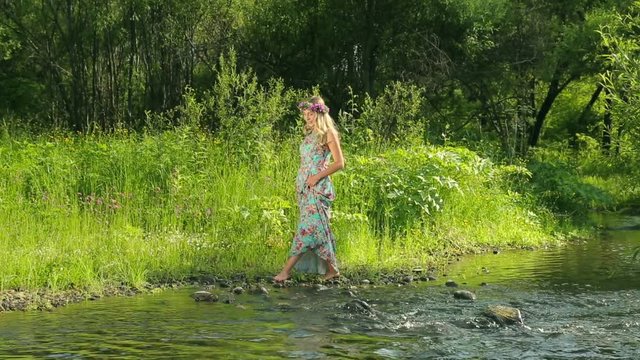 Young beautiful woman with flower wreath at the river. A beautiful girl walks by the river.