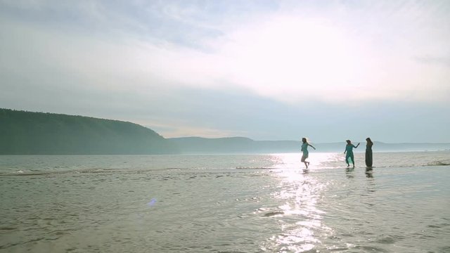 Party and people concept - group of smiling teen girls jumping on beach. Silhouette of three young women running around and jumping on the sandy beach at sunset.