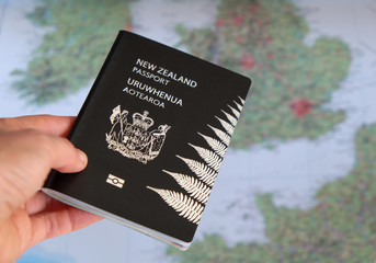 Hand holding a New Zealand NZ passport in front of a map of Europe.