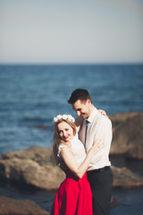 Romantic loving couple posing on stones near sea, blue sky