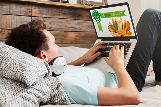 Man visiting a vegan restaurant website, lying at home.
