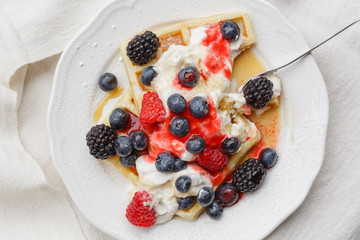 Waffles with raspberries, blueberries, whipped cream, berry fruit sauce and maple syrup