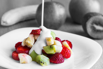 Healthy fruit salad with yogurt in white dish. Healthy breakfast, weight loss concept. Black and white image with colored fruit slices. Blurred background