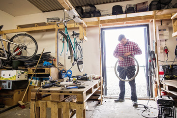 Full length of man repairing bicycle tire while standing at doorway in workshop