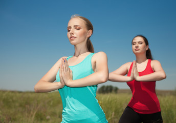 Two young women doing yoga outdoors on blue sky background