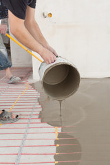 Fototapeta na wymiar Electric floor heating system installation in new house. Worker pouring concrete on the floor
