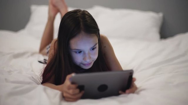 Little girl uses the tablet in bed before going to sleep