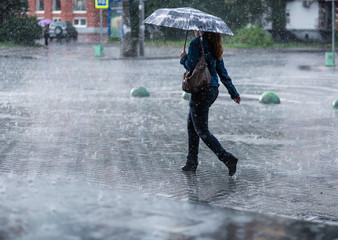 Woman with umbrella going on street during heavy rain .